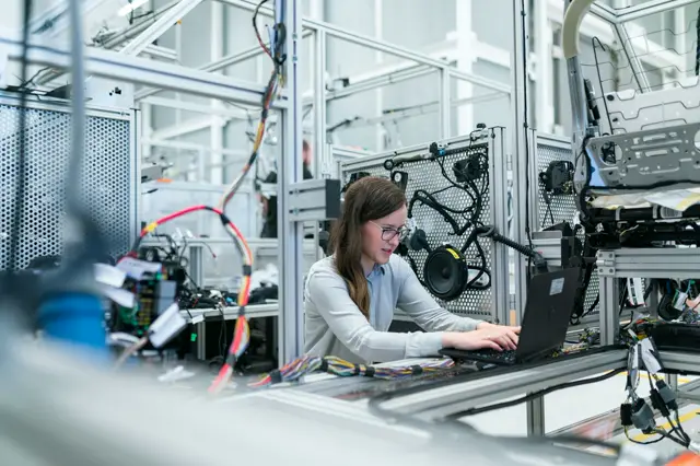 Engineer programming an automated production cell on a laptop