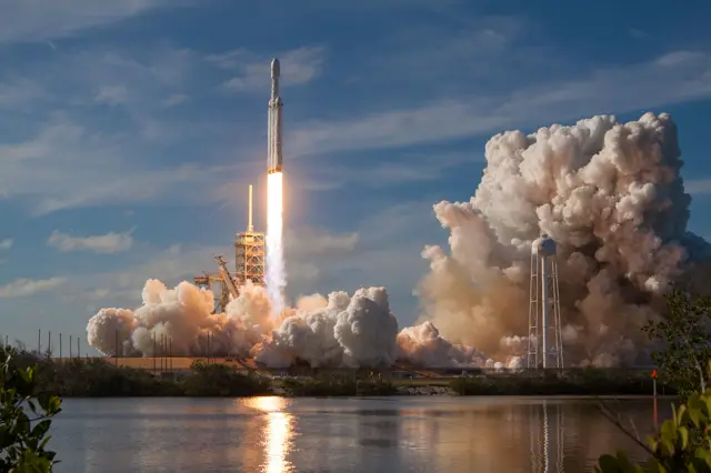 Rocket lifting off from its launch pad, reflected in the water